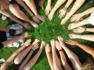 Photo of children's hands in the grass forming a circle