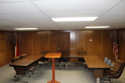 Inside the town hall meeting room.  Tables in a U shape with chairs around them and a podium